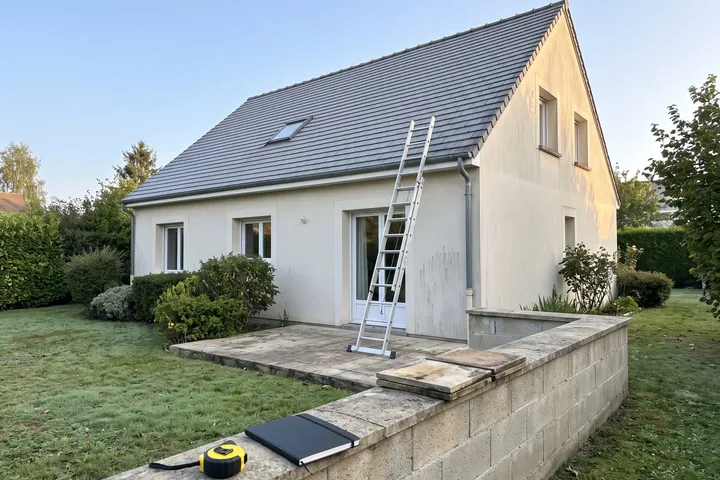 Une échelle contre la gouttière d'un pavillon, un mètre et un carnet sur le muret. Illustration.